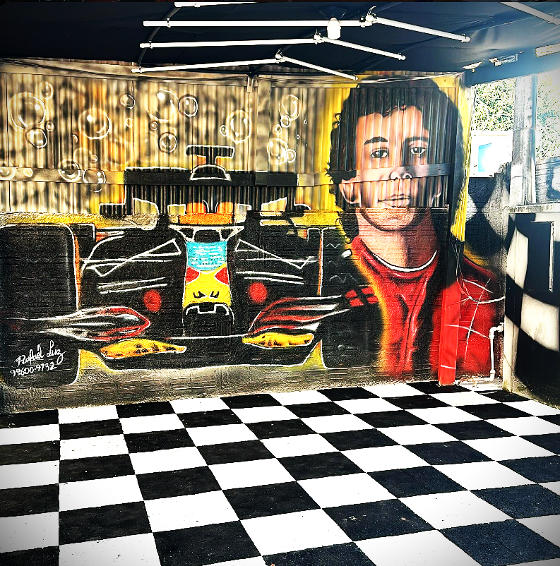Espaço da SALUCAR.LAVARAPIDO com mural de Ayrton Senna e carro de Fórmula 1, e piso quadriculado